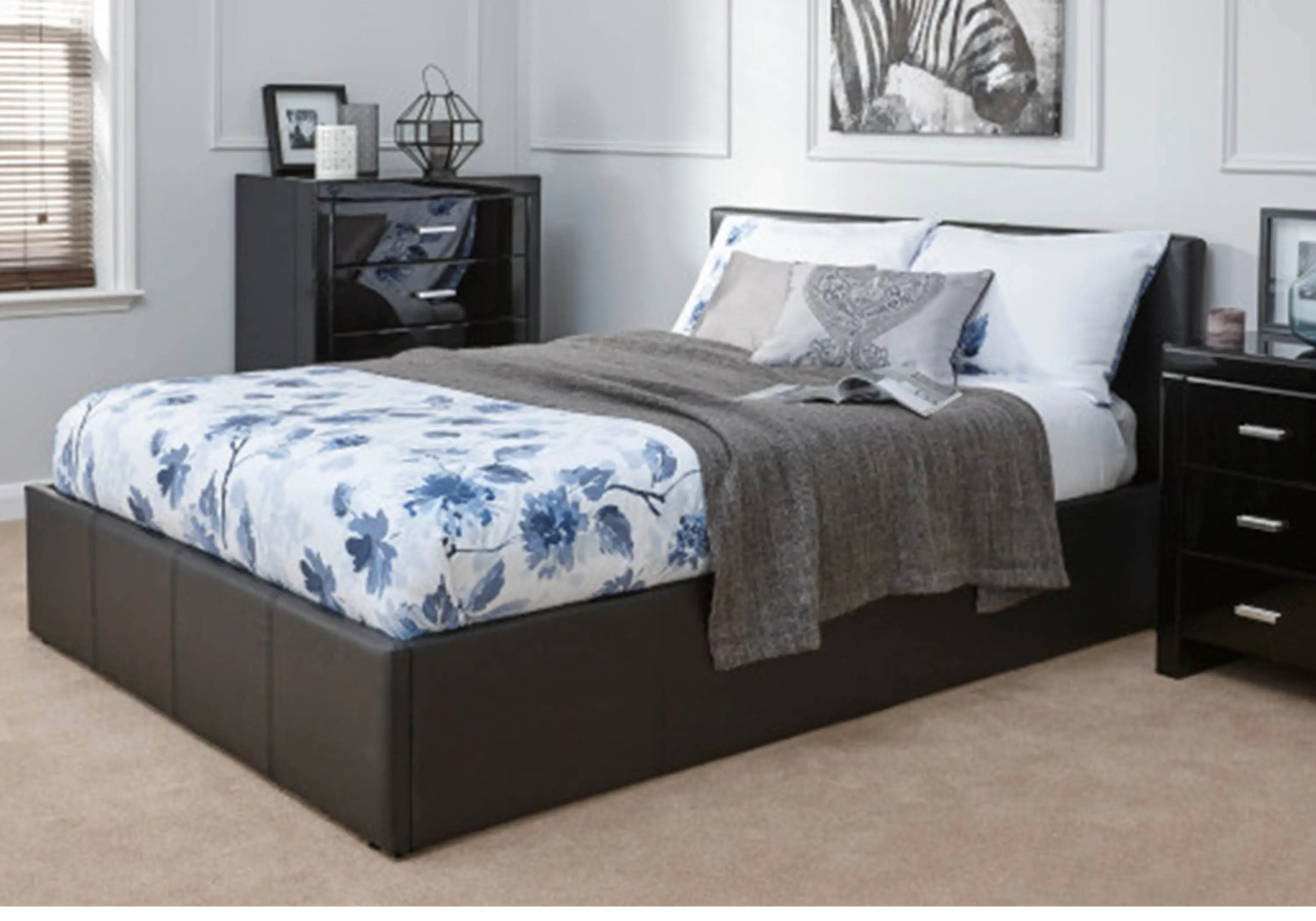 Black ottoman bed with white bedsheets, featuring blue flowery pattern, among black bedside furniture